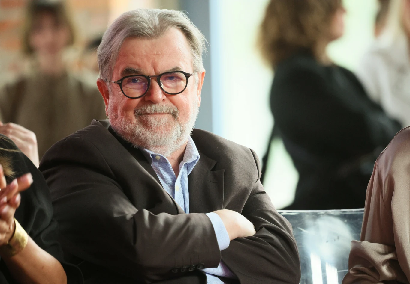 Edward Miszczak Edward Miszczak, starszy mężczyzna z siwą brodą i okularami w garniturze, siedzi z założonymi rękami.