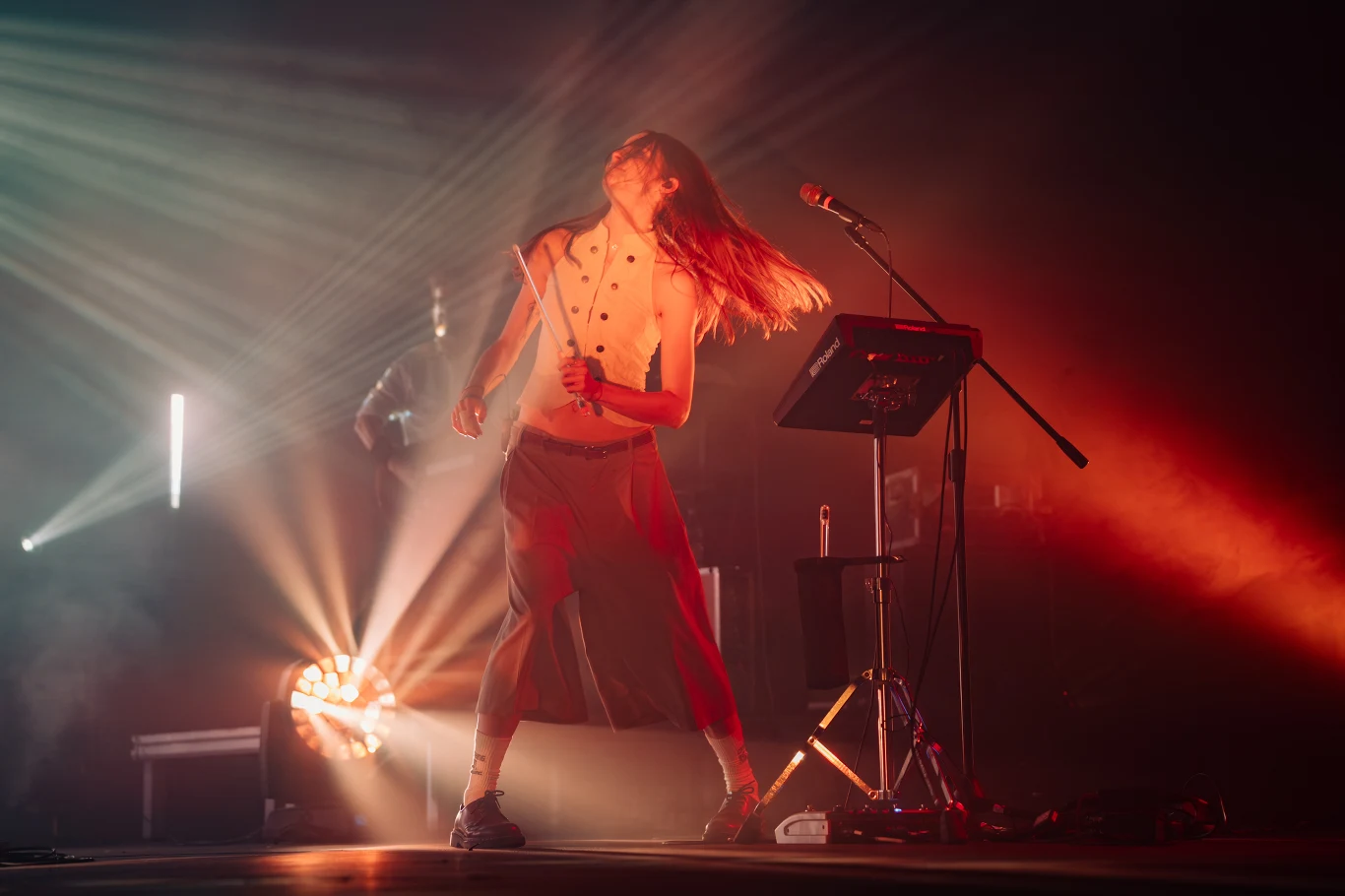 Festiwal FAMA: Daria ze Śląska Muzyk na scenie z pałeczkami perkusyjnymi w rękach, dynamiczne światła sceniczne i mikrofon ustawiony obok.