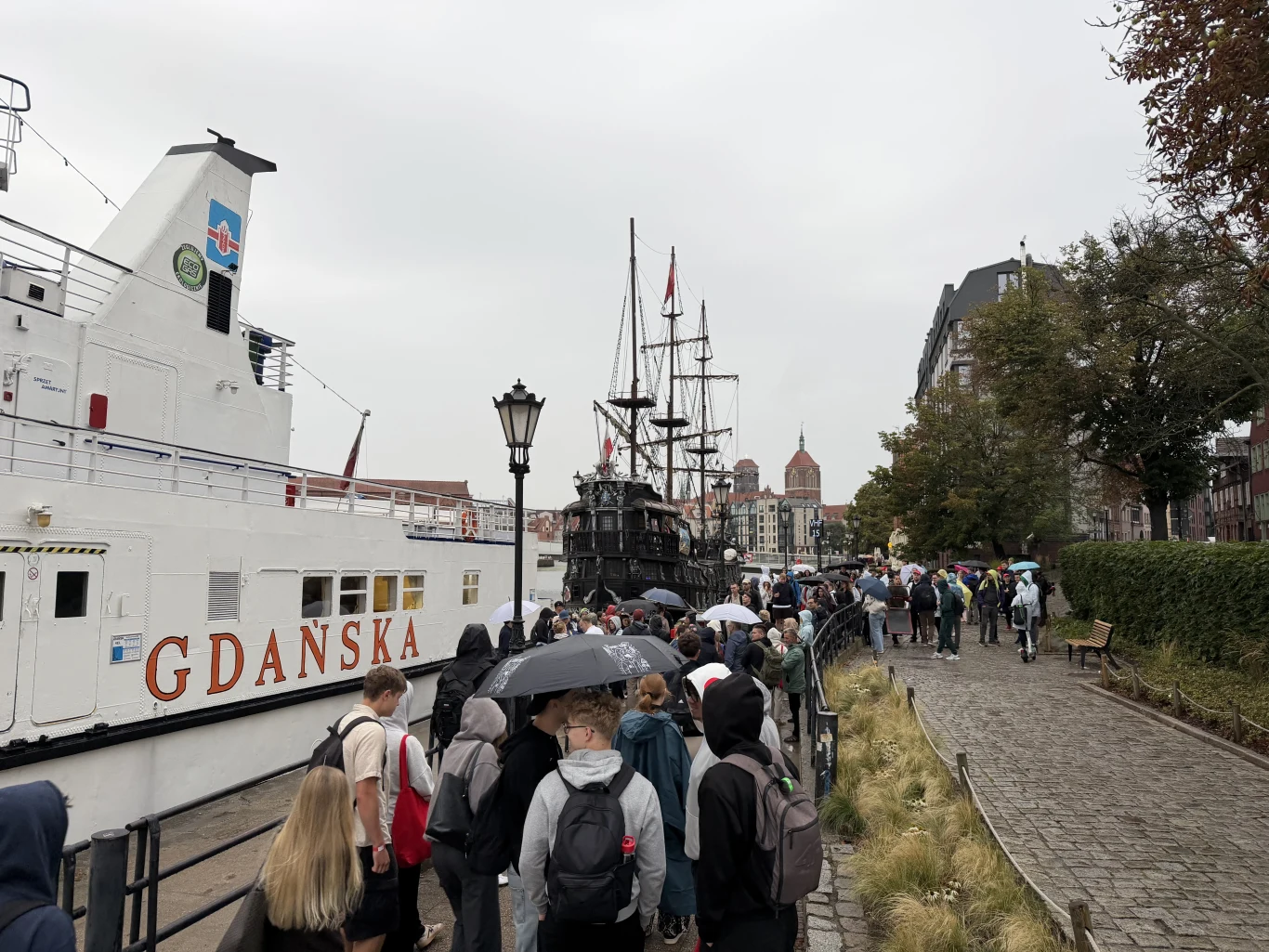 Gdańsk. Kolejka uczestników wydarzenia "Przyszłość.pl" przed wejściem na katamaran Tłum ludzi czekających w kolejce przy nabrzeżu obok statku o nazwie Gdańska oraz historycznego żaglowca, w tle zabudowania miasta i charakterystyczne wieże kościołów.