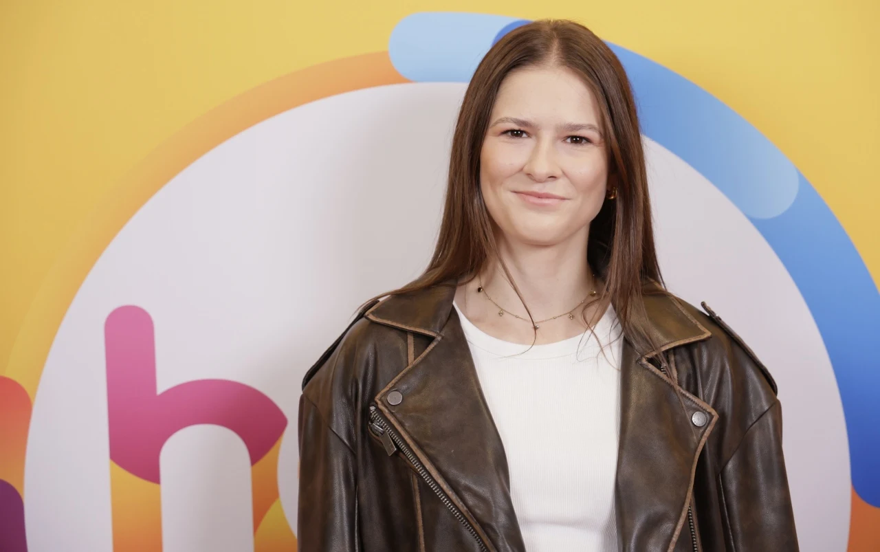 Pia Skrzyszowska w "halo tu polsat" Pia Skrzyszowska w białej bluzce i brązowej kurtce na tle kolorowej grafiki w studiu "halo tu polsat".