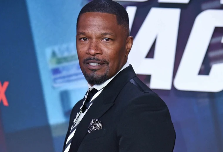 Jamie Foxx Jamie Foxx w garniturze stojący przed kolorowym banerem z dużymi białymi literami.