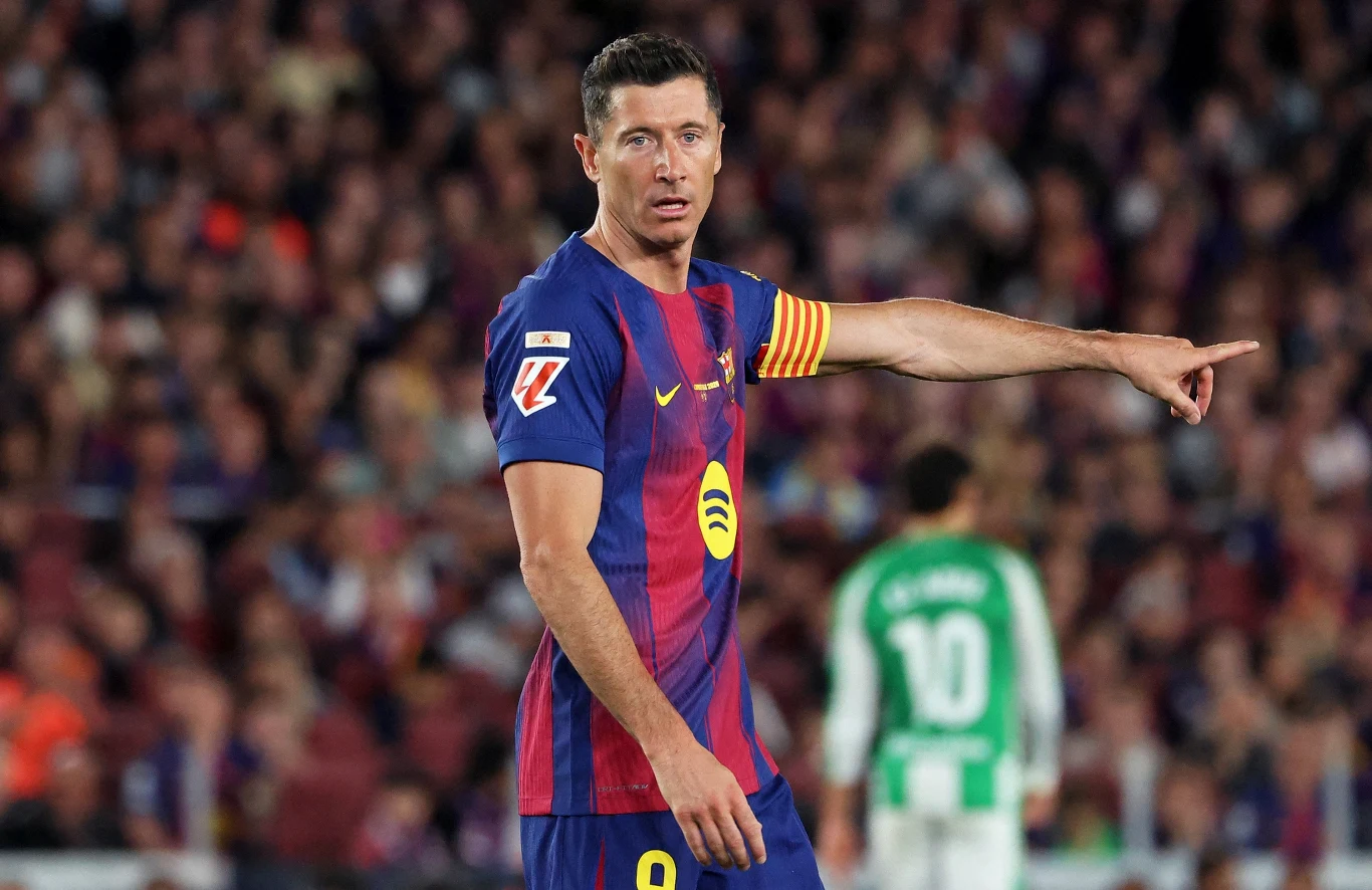 Robert Lewandowski Piłkarz w stroju FC Barcelony z opaską kapitana na ramieniu wskazuje ręką kierunek na boisku podczas meczu.