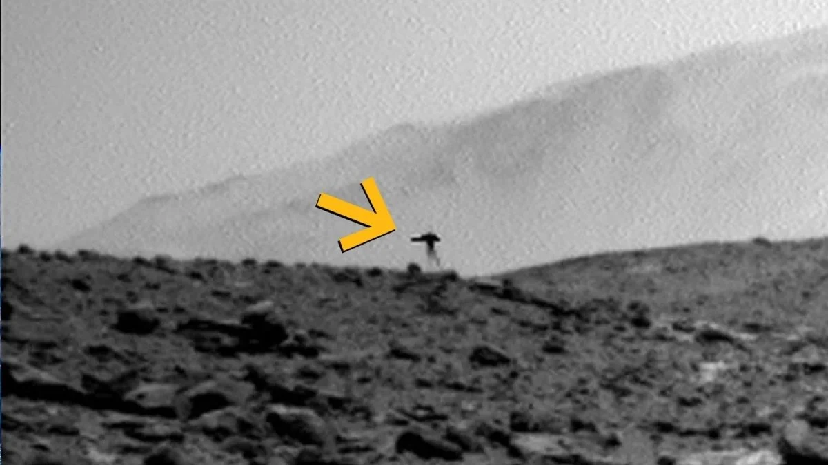 "Meduza" uchwycina przez łazik Curiosity na Marsie w 2023 r. Skalisty, pofałdowany teren z wyraźnym, kontrastującym ciemnym obiektem o nieregularnym kształcie, wskazanym przez żółtą strzałkę.