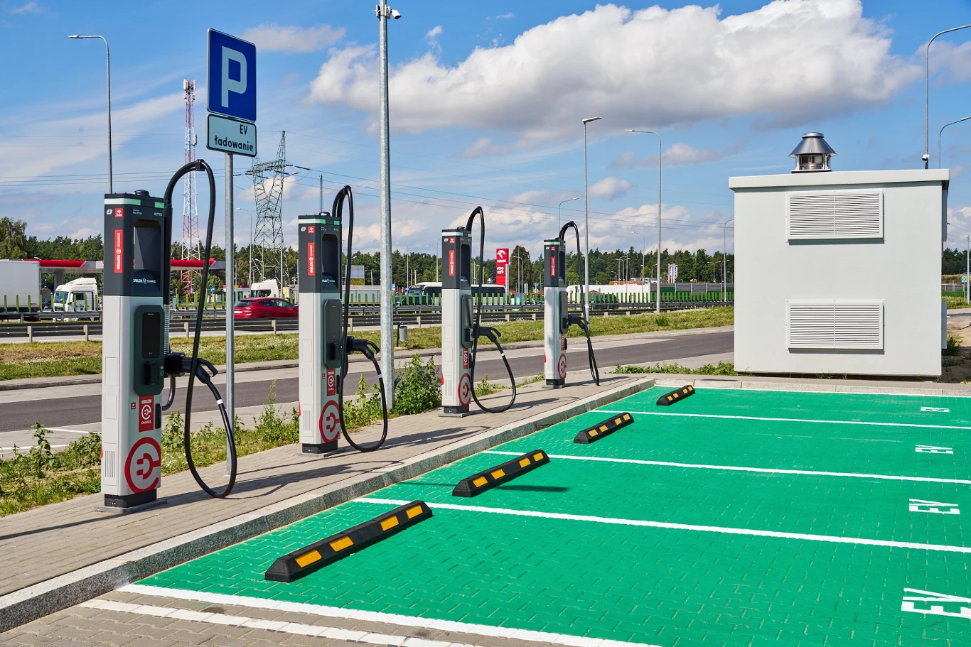Stacja ładowania samochodów elektrycznych z czterema słupkami ładowania oraz wyznaczonymi zielonymi miejscami parkingowymi.