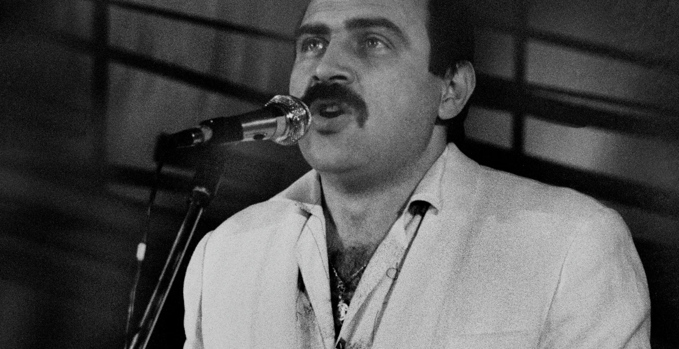 Andrzej Zaucha w Zielonej Górze w 1985 roku Andrzej Zaucha śpiewa do mikrofonu na scenie w Zielonej Górze, 1985 rok, jasna marynarka, wąsy.