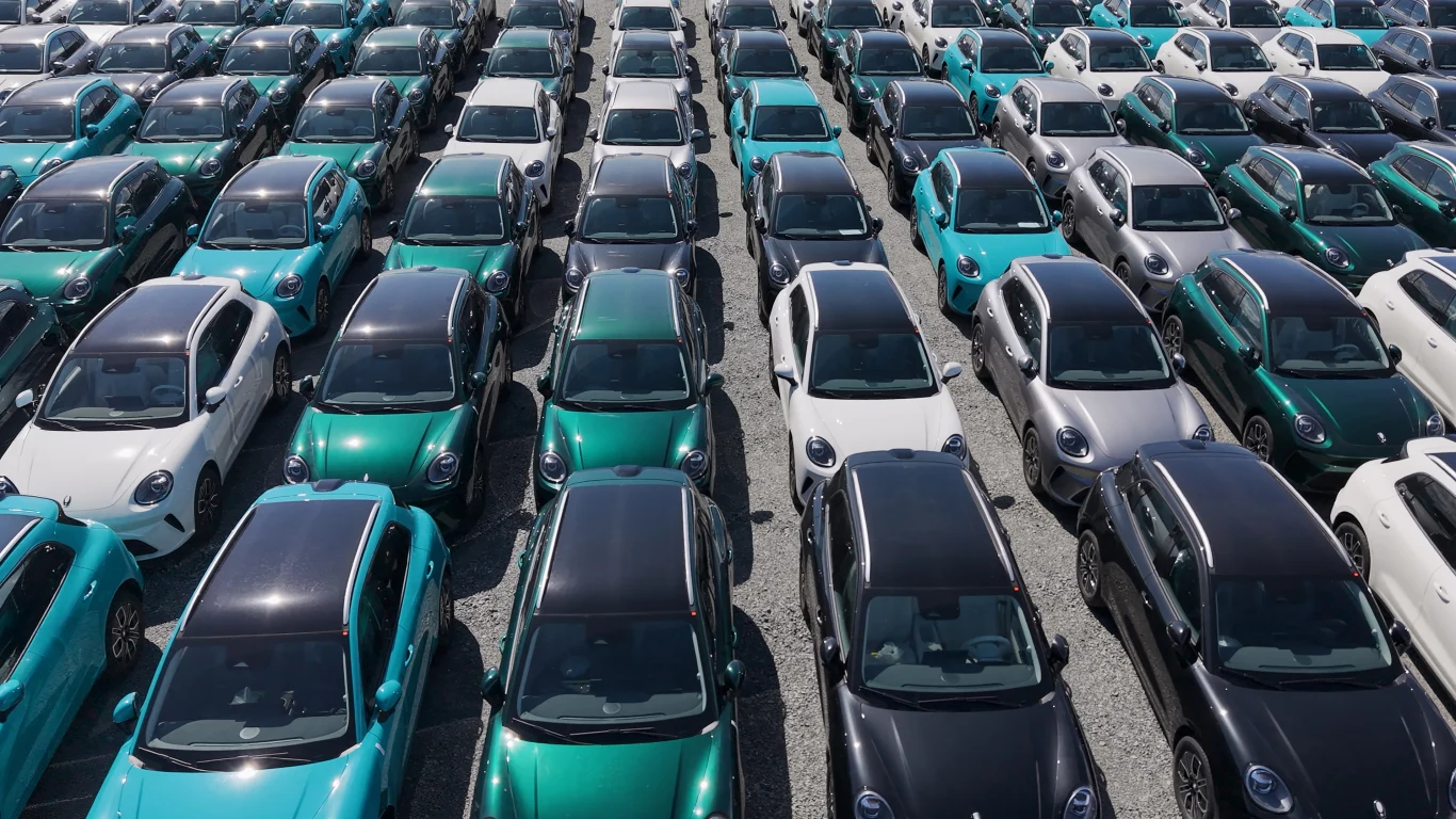 GMW Ora 5 to pierwszy model marki oferowany w Polsce Rzędy nowych samochodów w różnych odcieniach zieleni, bieli i szarości ustawione równolegle na dużym parkingu.