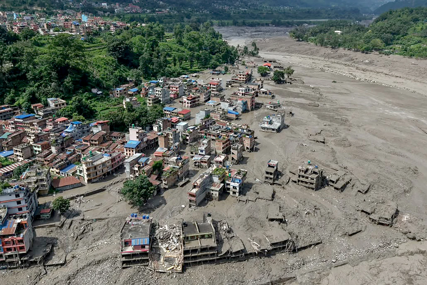 Skutki przejśćia fali powodziowej przez Trishuli Bazar w obwodzie Nuwakot w Nepalu Zrujnowane budynki wzdłuż koryta wyschniętej rzeki, osunięta ziemia i zniszczenia w bezpośrednim sąsiedztwie mieszkalnych zabudowań przy granicy lasu.
