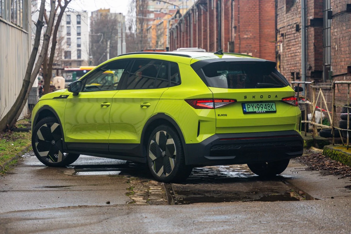 Skoda Elroq ma wszystko, by stać się podstawowym autem w rodzinie. Jaskrawo żółto-zielony SUV Skoda Enyaq na tle ceglanej zabudowy przemysłowej, z czarnymi akcentami i charakterystycznymi felgami.