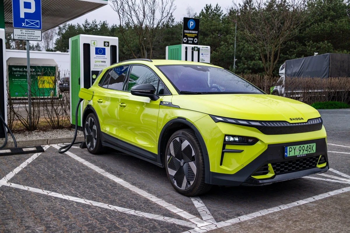 Maksymalna moc, z jaką można ładować baterię Elroqa to 185 kW. Jaskrawożółty samochód elektryczny marki Skoda podłączony do ładowarki na parkingu stacji ładowania, oznaczone miejsce dla pojazdów elektrycznych, w tle oznaczenia parkingowe i drzewa.