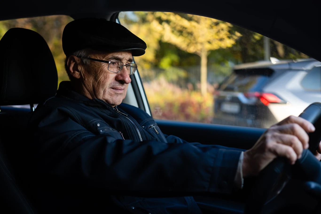 Najlepsze samochody dla seniorów. ADAC wybrał 10 modeli. Starszy mężczyzna w okularach i kaszkiecie prowadzi samochód, skupiony na jeździe.