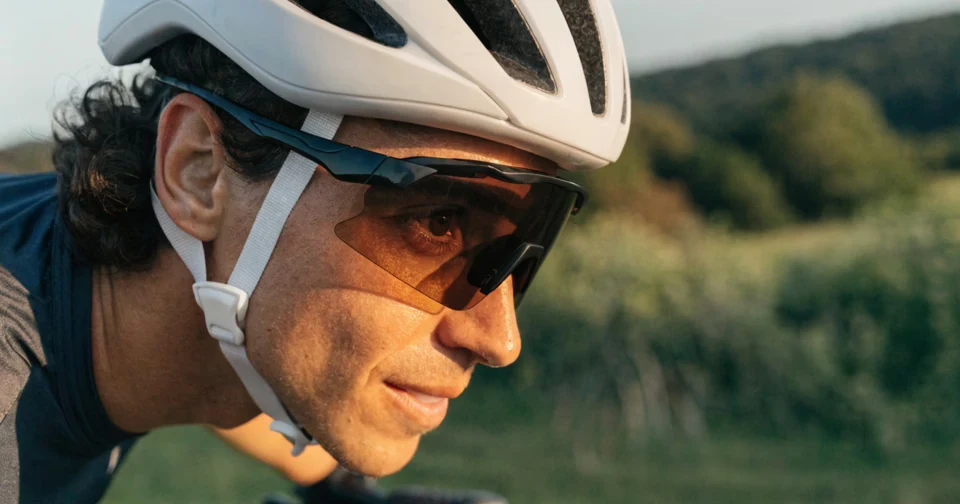 Mężczyzna w białym kasku rowerowym i sportowych okularach jadący na rowerze w plenerze.