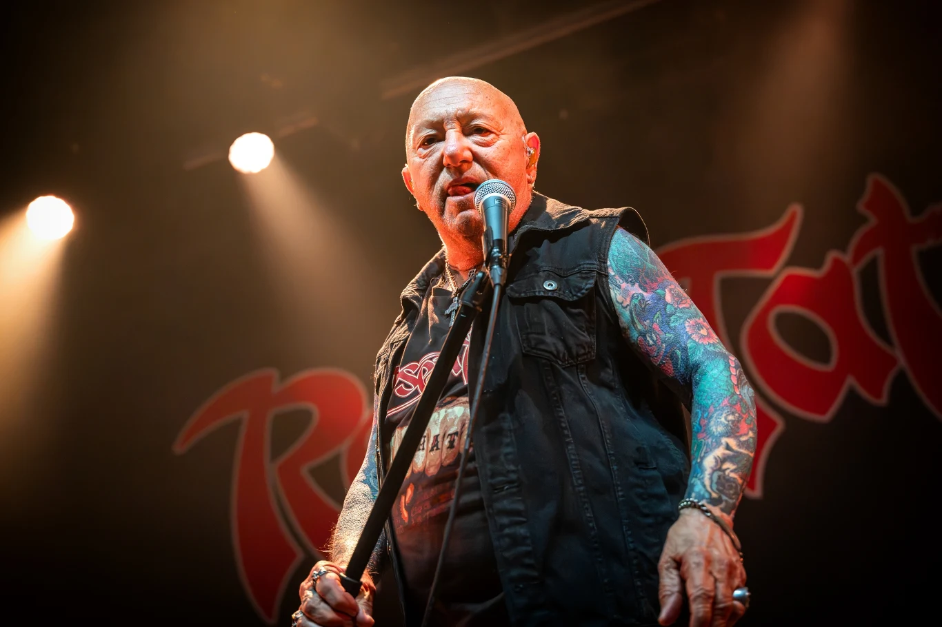 Angry Anderson (Rose Tattoo) przebywa w szpitalu w związku z poważnymi problemami zdrowotnymi Angry Anderson z Rose Tattoo śpiewa do mikrofonu na scenie, ubrany w czarną kamizelkę, widoczne tatuaże.