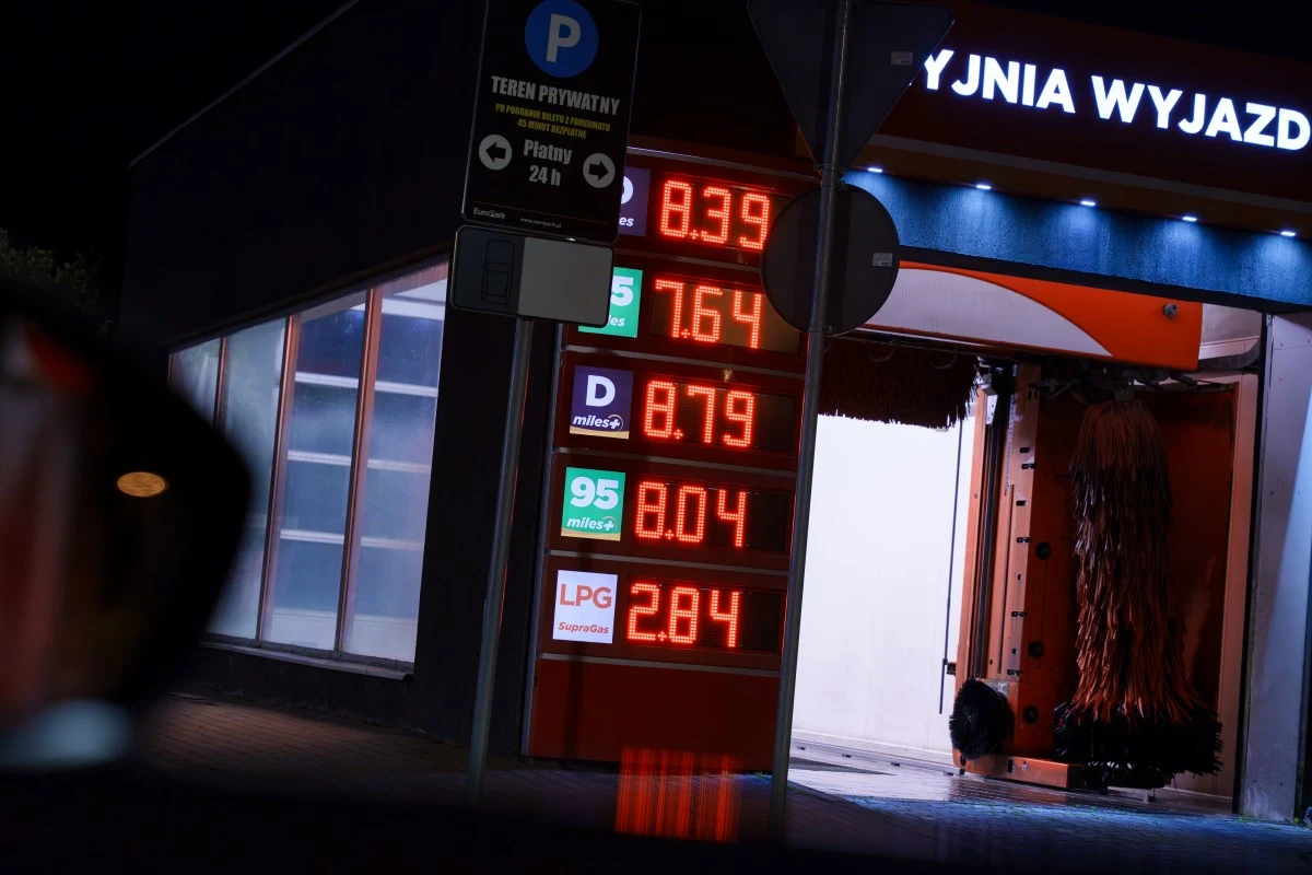 Cennik różnych rodzajów paliwa obok myjni samochodowej, wyświetlony na podświetlanej tablicy elektronicznej.