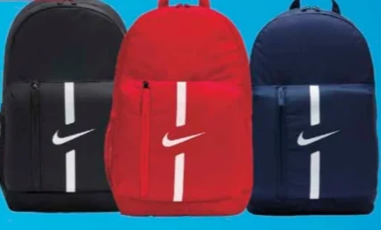 Trzy plecaki w kolorach czarnym, czerwonym i granatowym, każdy z białym logo Nike oraz pionowym białym paskiem na przedniej kieszeni.