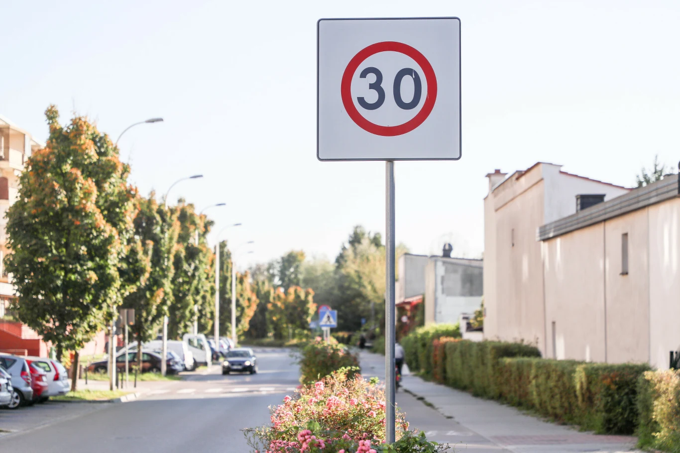 Co oznacza znak B-43? Jakie przepisy obowiązują kierowców? Znak B-43 ograniczenia prędkości do 30 km/h przy osiedlowej ulicy z budynkami i drzewami