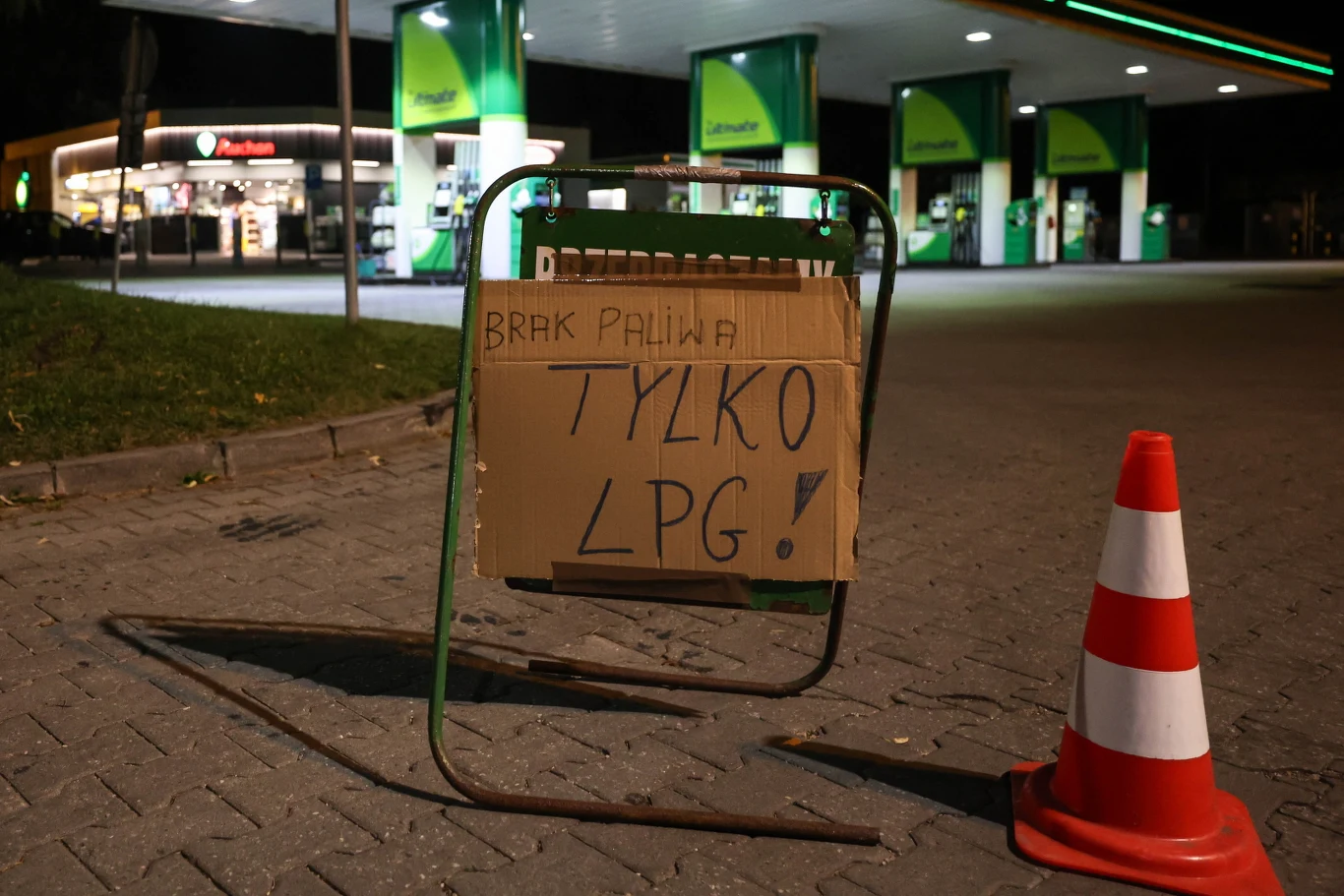 W poniedziałek stacje w całej Polsce przeżywały oblężenie, w efekcie na niektórych zabrakło paliwa Stojak z kartonową tablicą z napisem 'Brak paliwa, tylko LPG!' ustawiony przy parkingu stacji benzynowej, obok widoczny pachołek ostrzegawczy, w tle jasno oświetlone dystrybutory paliwowe.