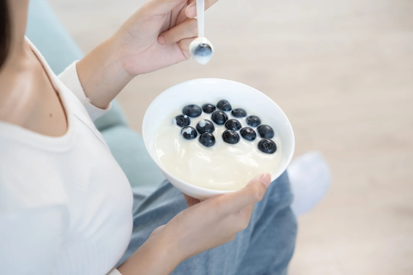 Najlepiej wybierać jogurt naturalny o krótkim składzie i wysokiej zawartości białka. Dobrze smakuje z owocami, orzechami i płatkami owsianymi Miska jogurtu naturalnego z borówkami trzymana w dłoniach, gotowa do spożycia łyżką.