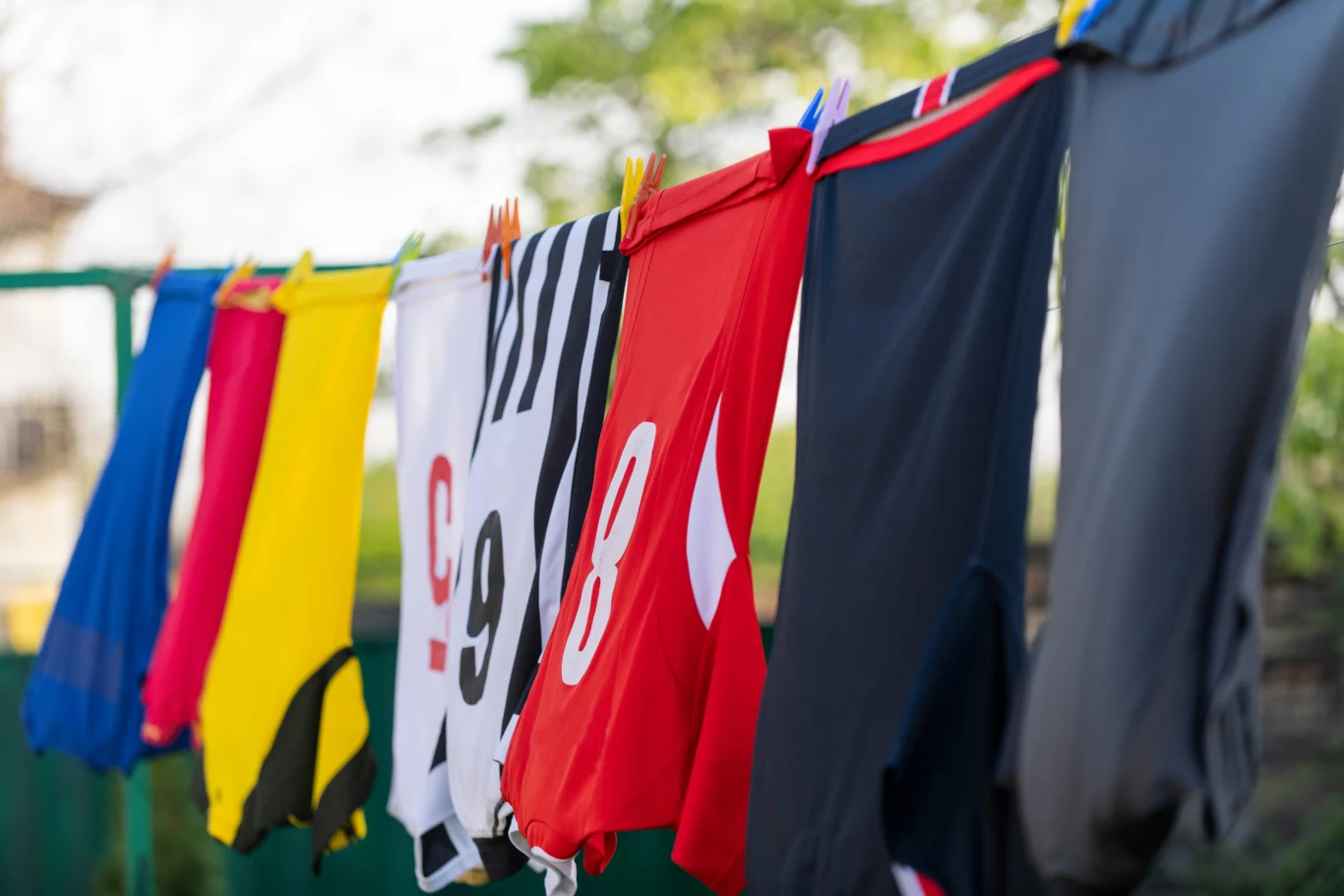 Kolorowe koszulki sportowe rozwieszone na suszarce za pomocą klamerek.