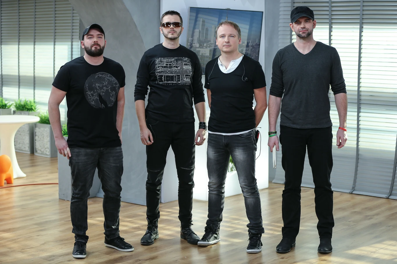 UFly w 2015 r., pierwszy z prawej Łukasz Ratuszny Czterech mężczyzn w ciemnych ubraniach stoi obok siebie na jasnej drewnianej podłodze, w nowoczesnym, dobrze oświetlonym pomieszczeniu z dużymi oknami w tle.