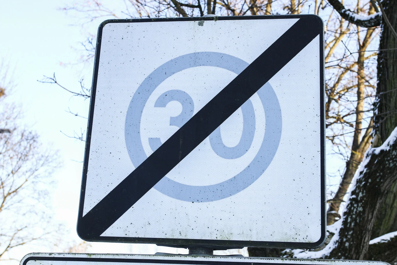 Znak drogowy B-44. Znak drogowy oznaczający koniec ograniczenia prędkości do 30 km/h, przekreślony czarnym pasem na tle śnieżnej scenerii.