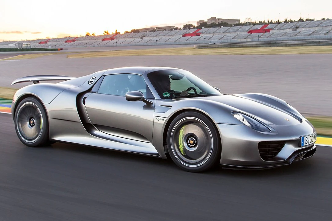 Porsche 918 Spyder zniknęło z rynku w 2015 roku Srebrny supersamochód Porsche 918 Spyder poruszający się po torze wyścigowym, niska i aerodynamiczna sylwetka, nowoczesny design, szerokie opony oraz masywne nadkola.