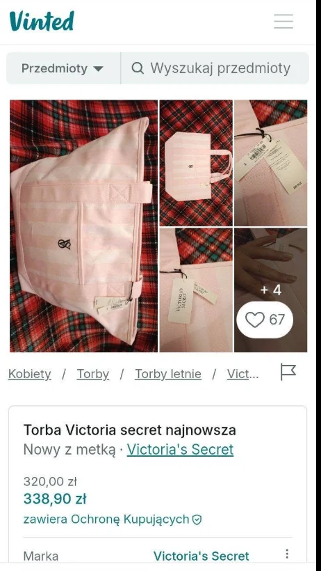 Różowa torba Victoria’s Secret z białą metką, wykonana z materiału, prezentowana na czerwonej kraciastej tkaninie, posiada oryginalny logotyp i rączki w tym samym kolorze.