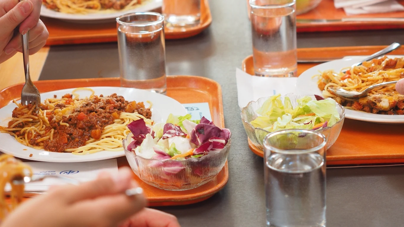 W polskich szkołach od 1 września 2026 r. ma królować dieta planetarna Talerze ze spaghetti z sosem mięsnym i porcją mieszanej sałaty, plastikowe tace oraz szklanki z wodą ustawione na stole.