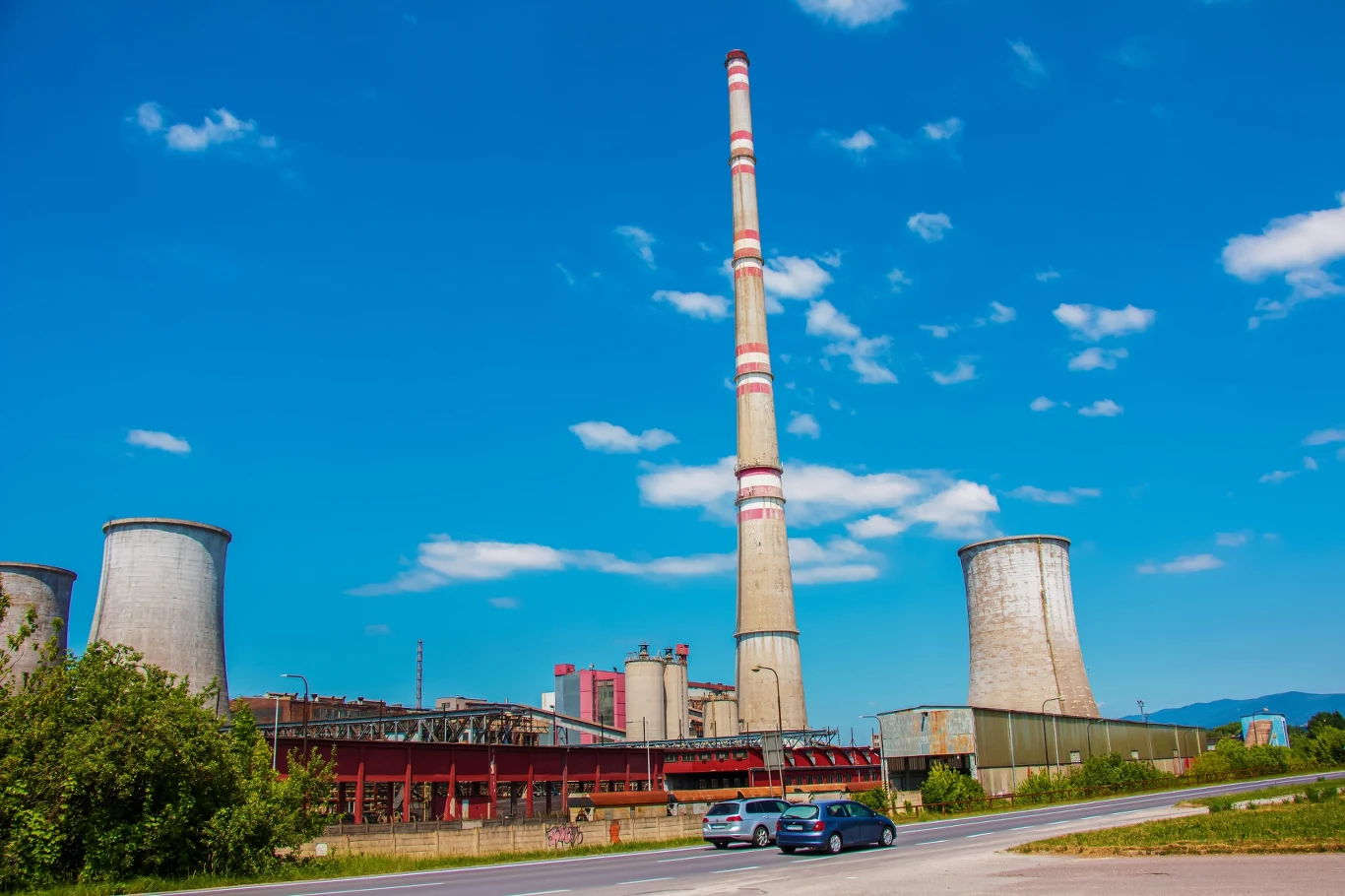 Niemcy dyskutują o możliwościach większego wykorzystania starych elektrowni węglowych. Zdj. ilustracyjne Komin przemysłowy i chłodnie kominowe starej elektrowni węglowej w Niemczech, na pierwszym planie samochody.