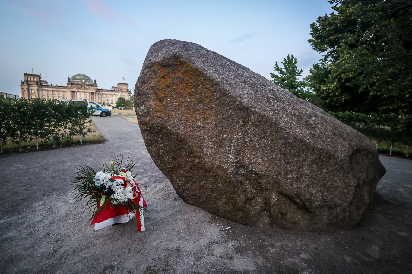 5 mln euro może kosztować pomnik polskich ofiar II wojny światowej Duży głaz na ziemi z biało-czerwoną wiązanką kwiatów i wstęgą, element tymczasowego pomnika w Berlinie.