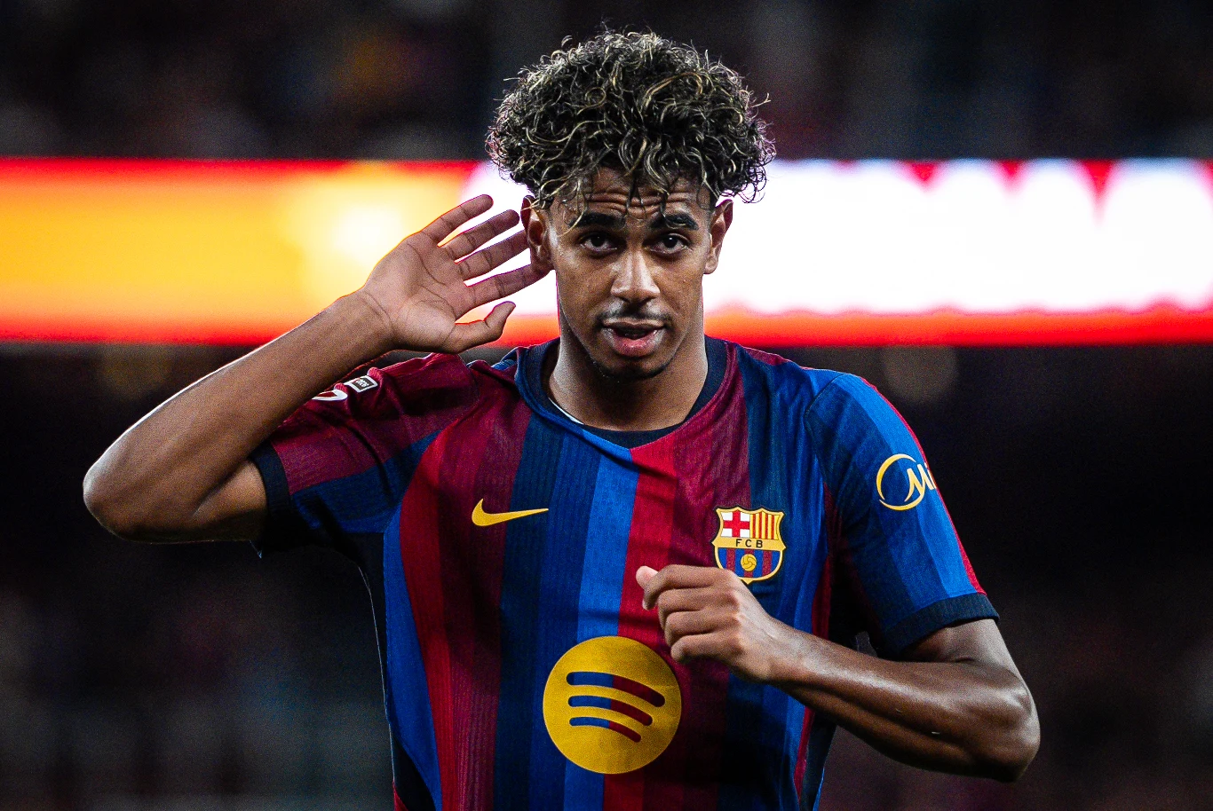Lamine Yamal Lamine Yamal w koszulce FC Barcelona wykonujący gest ręką przy uchu na boisku, skoncentrowany wyraz twarzy.