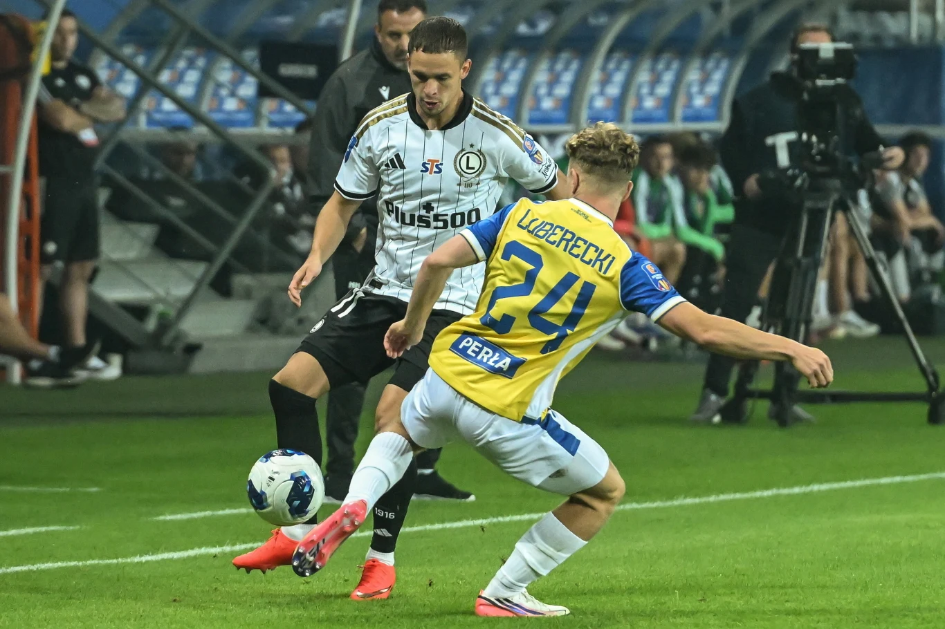Motor Lublin - Legia Warszawa w 1/32 STS Pucharu Polski Dwóch piłkarzy rywalizuje o piłkę podczas meczu na stadionie, jeden w biało-czarnej koszulce, drugi w biało-żółtej z numerem 24.