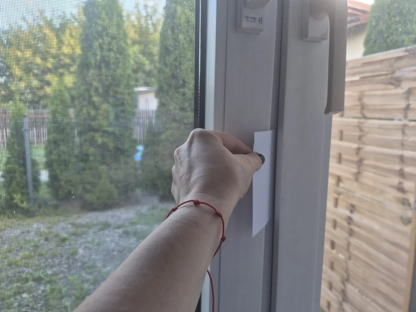 Prosty test z kartką pomoże nam w kilka chwil wychwycić miejsca, przez które okno może tracić szczelność. Kobieta wkłada kartkę papieru w szpary okna, by sprawdzić jego szczelność.