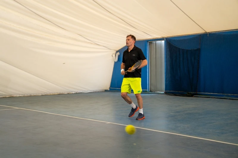 Jacek rzuci wyzwanie trenerowi Pauliny Mężczyzna w sportowym stroju z rakietą tenisową przygotowuje się do uderzenia piłki na krytym korcie tenisowym.