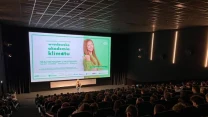 Duża sala kinowa zapełniona widzami, prelegent stojący przed dużym ekranem wyświetlającym plakat wydarzenia 'wrocławska akademia klimatu', z widoczną młodą kobietą i zieloną kolorystyką grafiki.