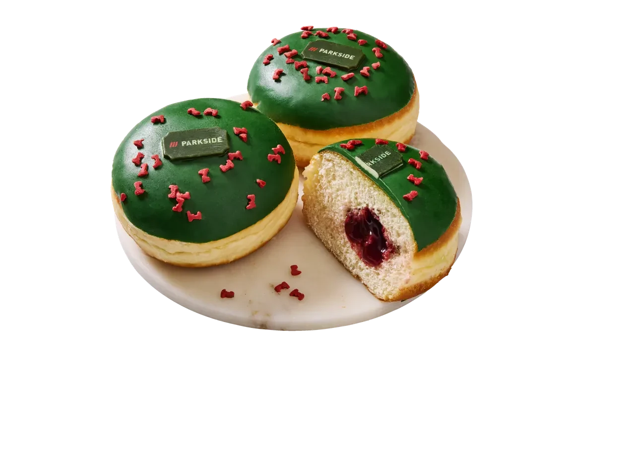 Pączek Parkside Trzy pączki z zieloną polewą, posypane małymi czerwonymi ozdobami, z czego jeden przekrojony ukazujący nadzienie wiśniowe, na dwóch z nich widoczny prostokątny opłatek z logo Parkside.