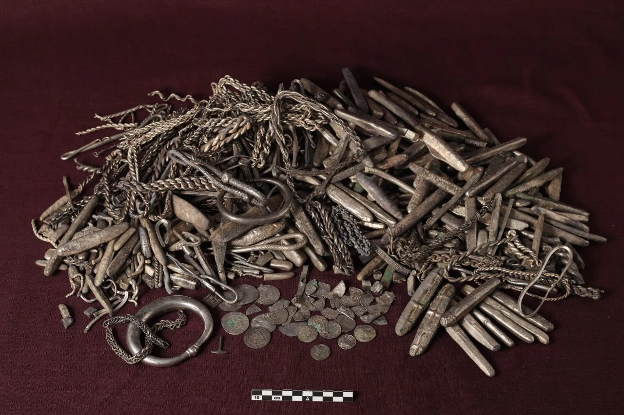 Największy taki skarb w Danii. Odkrył 18,5 kg srebra wikingów, które przeleżało w ziemi ponad 1100 lat Skarb wikingów: srebrne ozdoby, bransolety, sztabki i monety na ciemnej tkaninie z podziałką pomiarową.