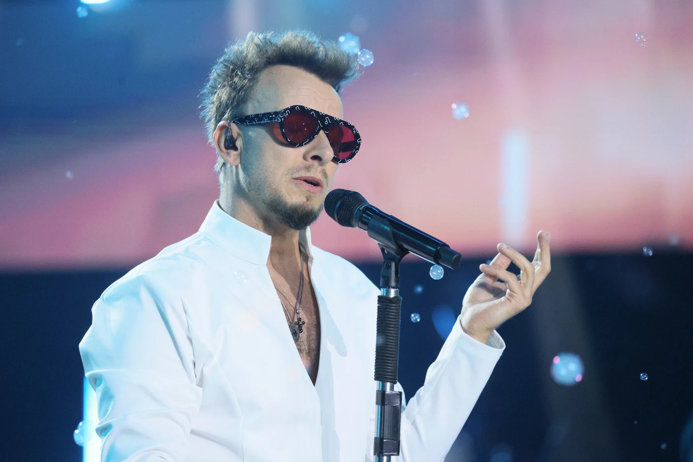 Piotr Kupicha (Feel) podczas Magicznego Zakończenia Wakacji w Kielcach Piotr Kupicha w białej koszuli i okularach śpiewa do mikrofonu na scenie z bańkami mydlanymi.