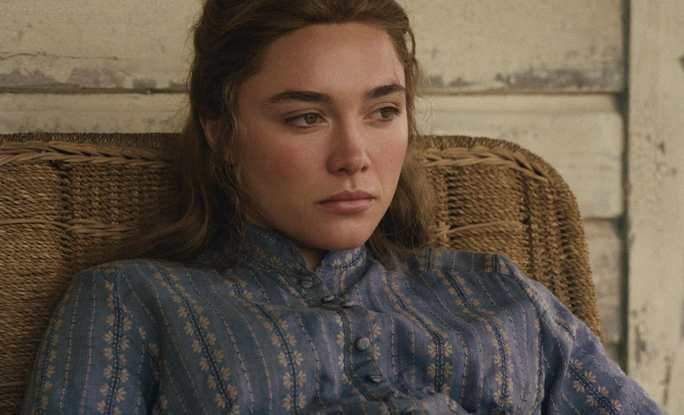 "Na wschód od Edenu" Florence Pugh jako młoda kobieta na wiklinowym fotelu, w niebieskiej bluzce, na tle jasnej, drewnianej ściany.