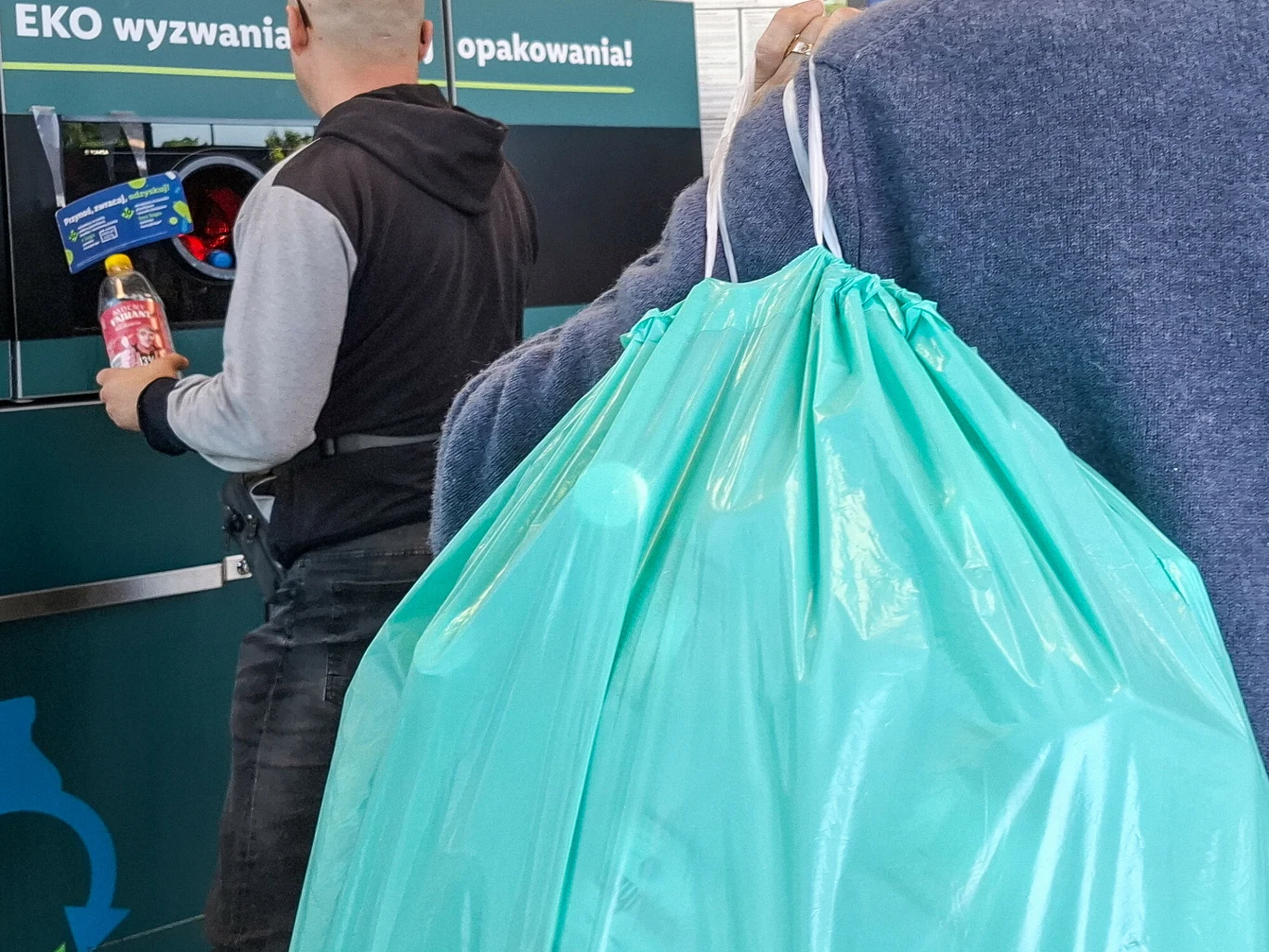 Dwie sieci sklepów zdecydowały się wydłużyć ważność bonów w systemie kaucyjnym do 90 dni Osoba wrzuca plastikowe butelki do recyklomatu, obok duża torba z pustymi opakowaniami.