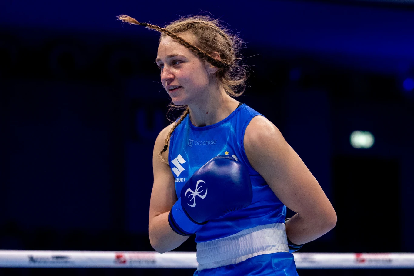 Julia Szeremeta Julia Szeremeta ubrana w niebieski strój bokserski stoi w ringu z uniesionymi rękawicami i uśmiechem na twarzy.