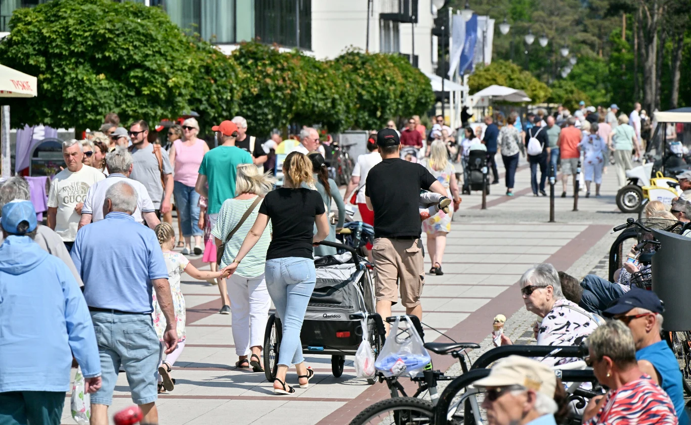 Mieszkańcy Świnoujścia sprzeciwiają się kolejnym wysokim budynkom w reprezentatywnej części miasta. Tłum spacerujących ludzi na promenadzie w Świnoujściu otoczony zielenią i miejskimi budynkami.