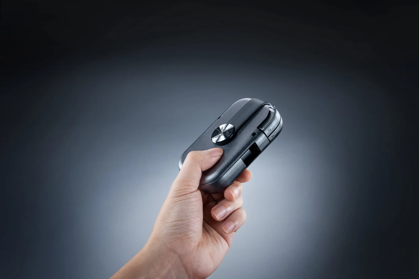 Razer Prio Ręka trzymająca niewielkie, składane urządzenie elektroniczne z widocznym srebrnym przyciskiem pośrodku obudowy.
