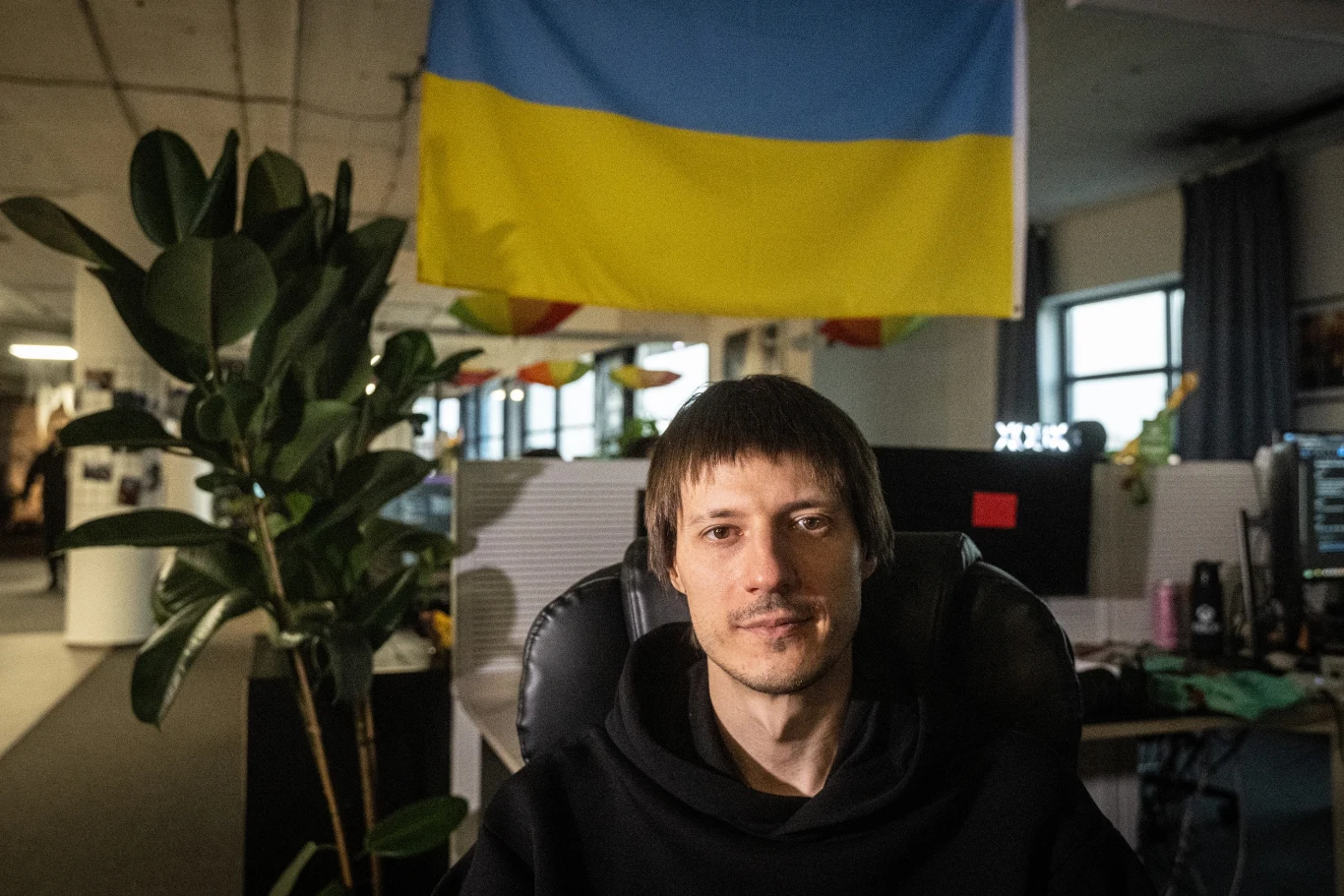 Ievgen Grygorovych, CEO studia GSC Game World w siedzibie zlokalizowanej w Pradze Mężczyzna siedzący na krześle biurowym w nowoczesnym wnętrzu, za nim powieszona ukraińska flaga oraz duża roślina w doniczce po lewej stronie kadru.