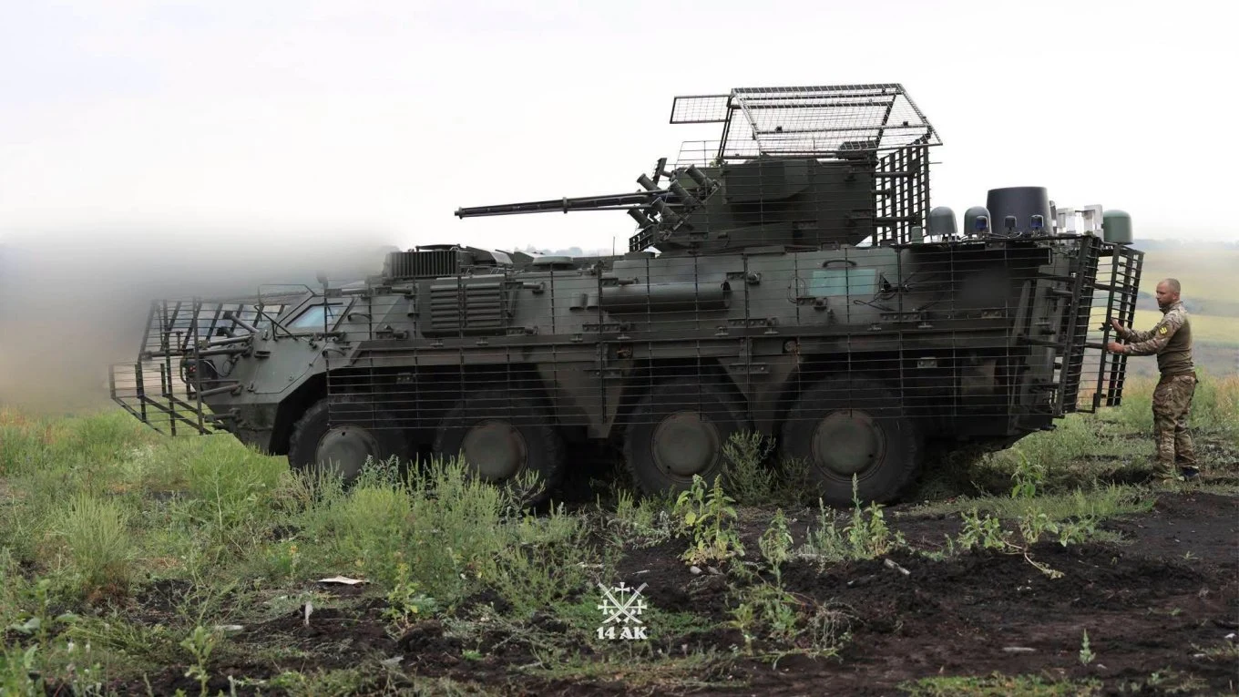 "Bucefał" na poligonie. Ukraińskie załogi testują transporter opancerzony BTR-4E BTR-4E Bucefał na trawiastym poligonie, transporter opancerzony z wieżyczką i żołnierz obok pojazdu.