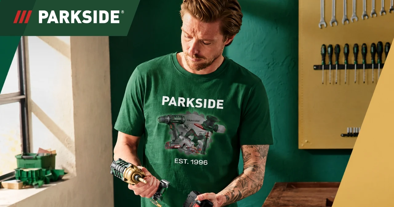 PARKSIDE mocno rozszerza ofertę. Ubrania i buty dla majsterkowiczów od 14,99 zł w Lidlu i Kauflandzie Mężczyzna w zielonej koszulce Parkside z logo trzyma narzędzie, za nim tablica z narzędziami i kluczami.