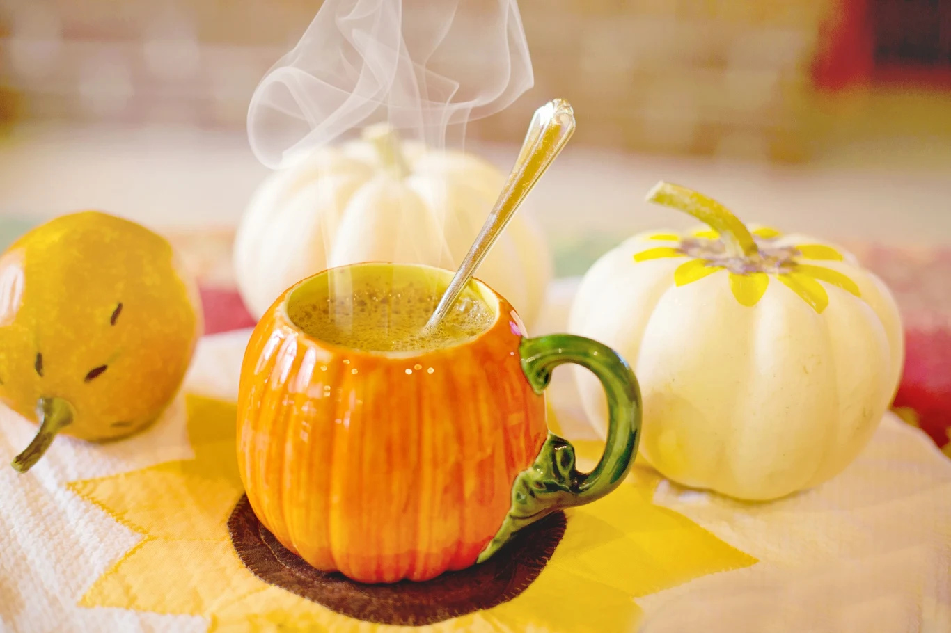 Domowy syrop pumpkin spice pomoże odwzorować kultową kawę, a przy tym nie dostarczy dużo kalorii Domowy syrop pumpkin spice, pomarańczowy kubek w kształcie dyni z kawą i łyżeczką, dwie białe dynie obok.