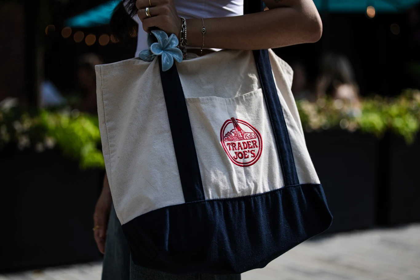 Wygląda niepozornie, a stała się globalnym fenomenem Osoba w jasnym topie trzyma dużą płócienną torbę z granatowymi uchwytami i czerwonym logo Trader Joe's.