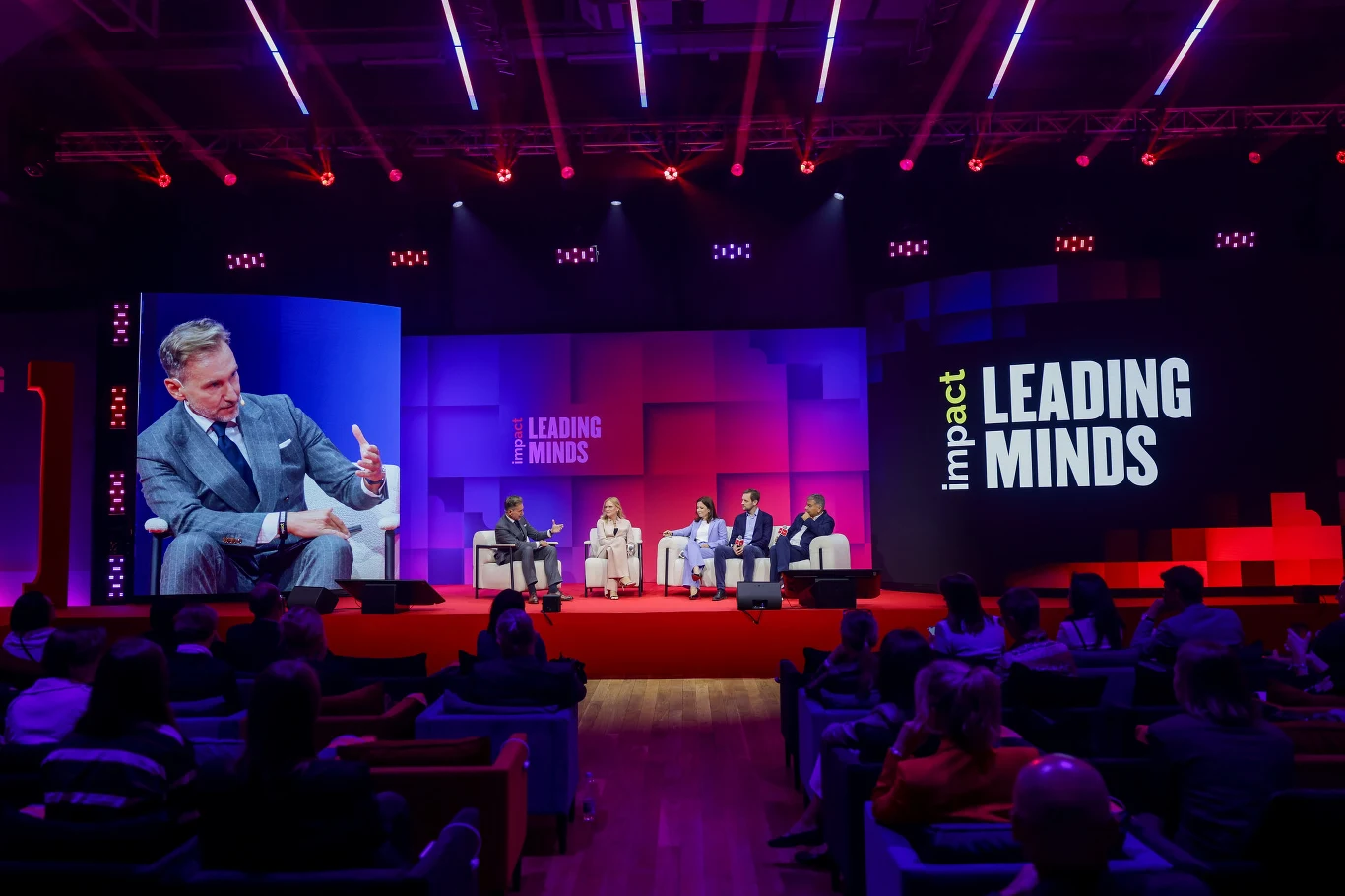 Panel dyskusyjny z udziałem pięciu prelegentów siedzących na scenie na tle dużego ekranu z napisem 'impact LEADING MINDS', z liczną publicznością obserwującą wydarzenie.
