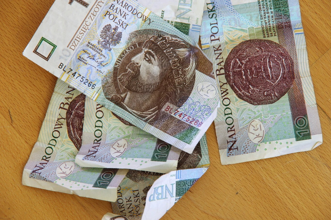 Unikatowy banknot o nominale 10 zł został sprzedany na aukcji za ogromną kwotę. Zdjęcie ilustracyjne. Rozrzucone banknoty 10 zł z wizerunkiem Mieszka I na drewnianym blacie, zdjęcie ilustracyjne.