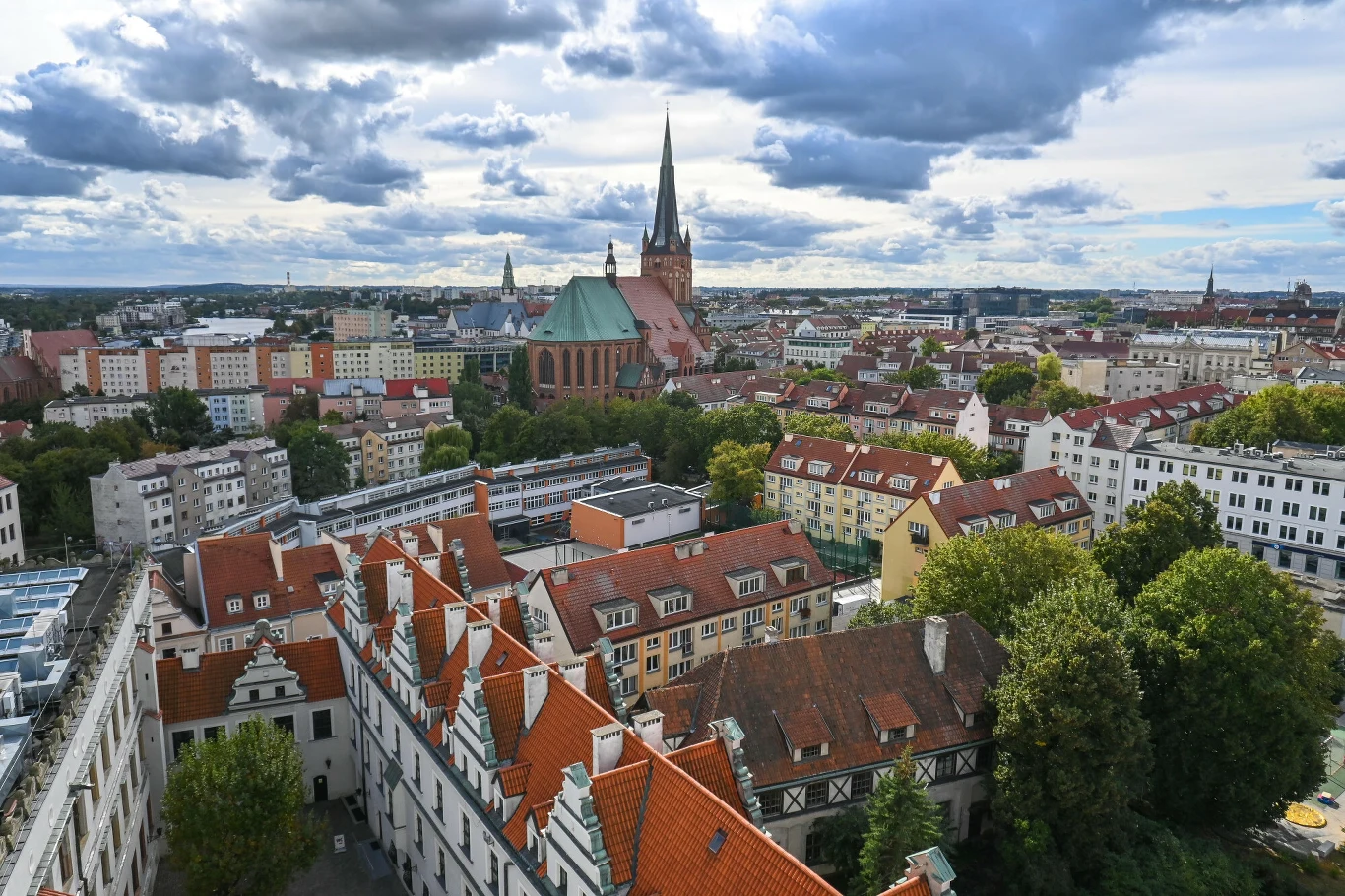 Panorama miasta z widoczną zabudową o czerwonych dachach, dominująca katedra z wysoką wieżą oraz otoczenie zieleni i niskich bloków mieszkalnych.